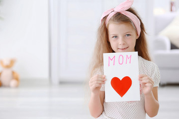 Cute girl with handmade greeting card for mother at home
