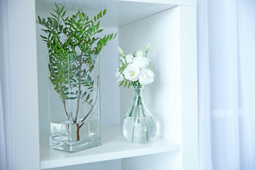 Beautiful flowers in glass vases on white shelf