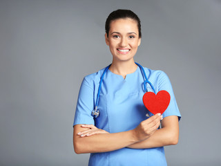 Portrait of doctor cardiologist with red heart in hand on grey background