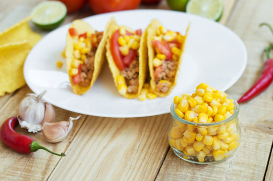 Ingredients for mexican tacos: yellow corn, chili pepper, garlic, crispy taco shells, lime and tomatoes