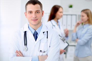 Fototapeta premium Friendly male doctor on the background with patient in hospital. High level and quality medical service concept.