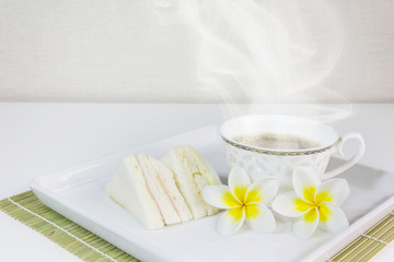 Cup of hot coffee with sandwich and flower