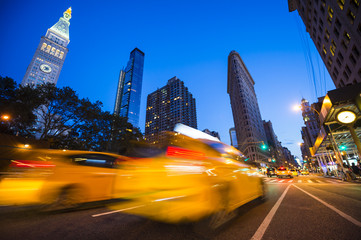 Defocus motion blur view of yellow taxis driving through the city streets at dusk in New York City, USA
