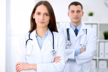 Fototapeta premium Young beautiful female doctor smiling on the background with patient in hospital. High level and quality medical service concept.
