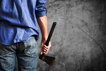 A guy holding old rusty axe, close up rear view, on dark concrete texture background with copy space