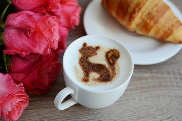 cup of cappuccino and yummy croissant with roses on the table