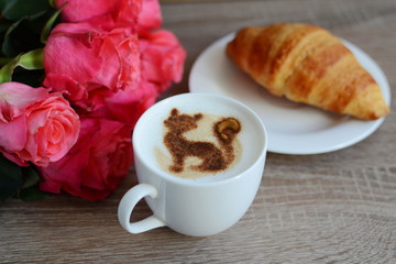 cup of cappuccino and yummy croissant with roses on the table