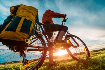 Hiker with loaded bicycle on a green summer meadow at sunset