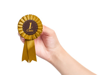 hand holding golden first class rosette on white background