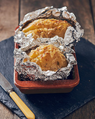 jacket potatoes with provola cheese wrapped in an aluminium foil on a slate plate