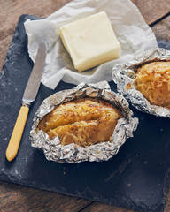 jacket potatoes with provola cheese wrapped in an aluminium foil on a slate plate