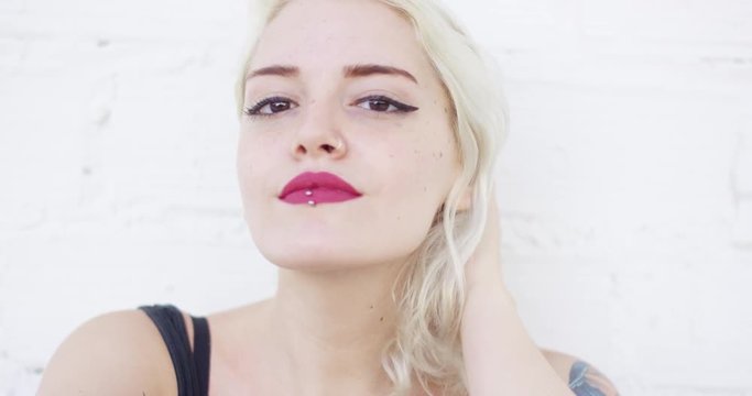 Attractive blond woman with a lip piercing wearing red lipstick smiling quietly at the camera  close up frontal head and shoulders