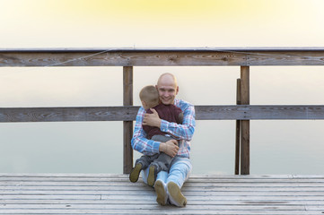 Father and baby son sitting on the wooden bridge.