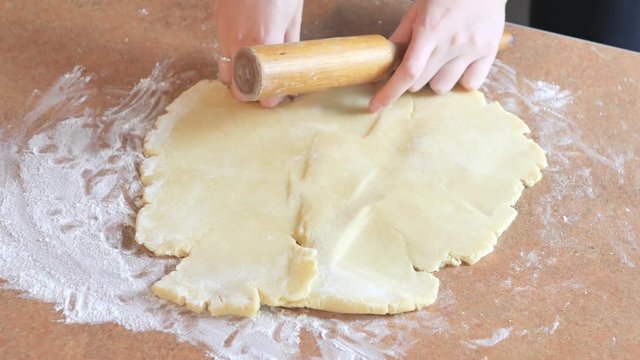 Baker kneading dough with rolling pin on table prepares bread or apple pie