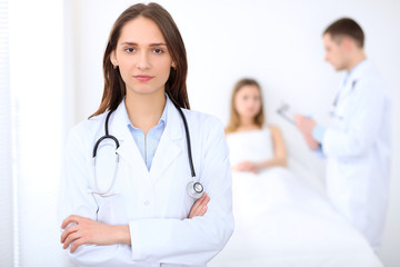 Fototapeta premium Friendly female doctor on the background with patient in the bed and his physician