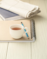 Hot tea cup on a notebook on a white wooden table.