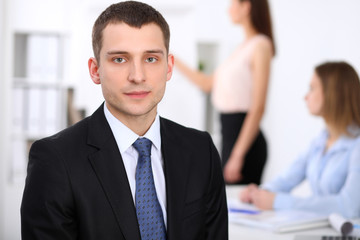 Portrait of a young business man  against a group of business people at  meeting.