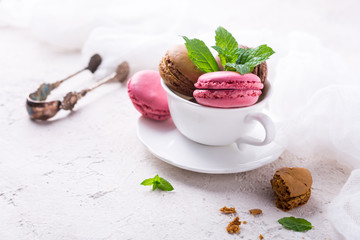 Colorful almond cookies macaron or macaroon in white coffee cup on light background, vintage card, holiday food concept, copy space for text.