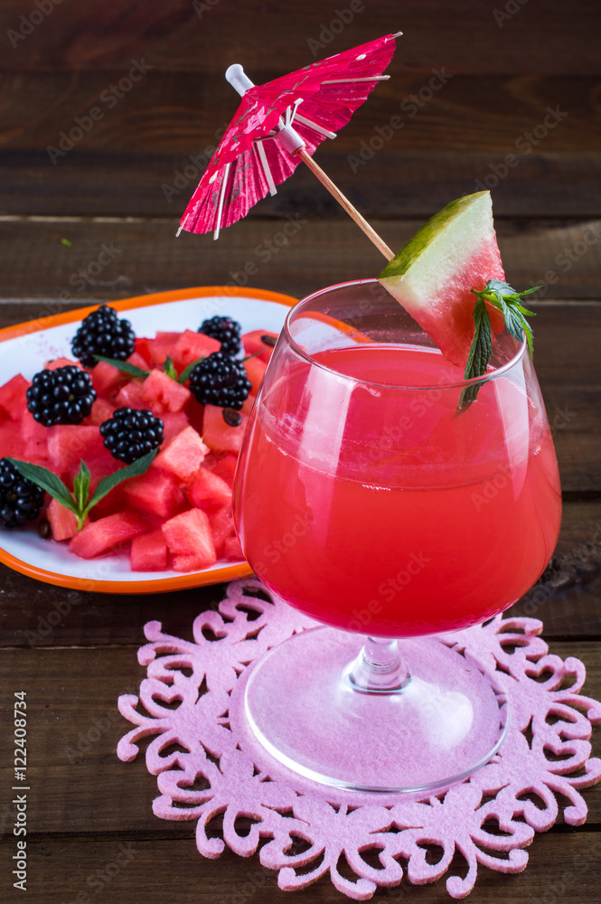 Poster Watermelon fresh in a glass with an umbrella, a salad of watermelon, blackberry and mint. On a wooden background.