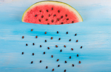 A cloud of slices of watermelon. A rain of seeds. On a wooden blue background.