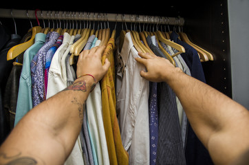Man searching for a shirt hanging on the rail in his wardrobe, first person point of view looking...