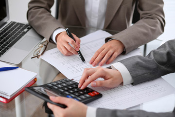 Two female accountants counting on calculator income for tax form completion hands closeup....