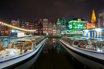 Fototapeta premium Beautiful typical Dutch dancing houses, Oude Kerk church and tourist boats at the Amsterdam canal Damrak at night, Holland, Netherlands.