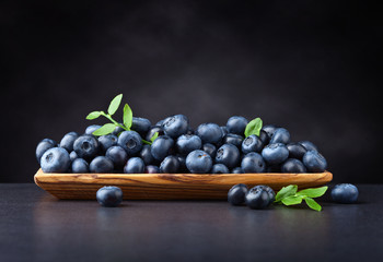 blueberries with green leaves in wooden dish