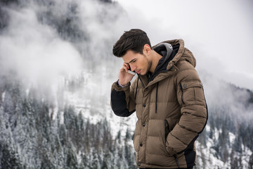 Dark haired handsome young man in winter outerwear using cell phone or smartphone, outdoor at...