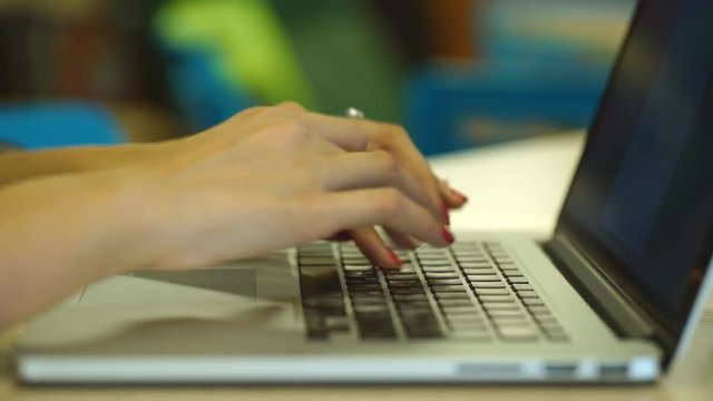 Close-up of female hands typing text message on laptop indoors, young female student sitting on the library stairs and using portable computer