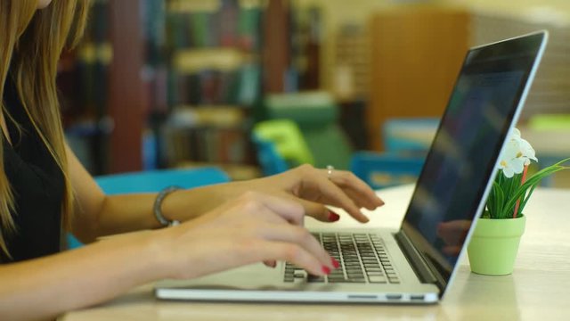 Close-up of young female student sitting on the library stairs and using portable computer