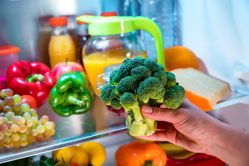 Woman takes the broccoli from the open refrigerator.