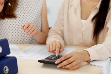 Two female accountants counting on calculator income for tax form completion hands closeup. Internal Revenue Service inspector checking financial document. Planning budget, audit  concept