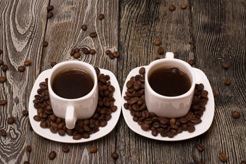 two small white cups of coffee with cocoa beans on wooden background