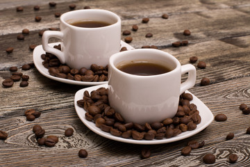 two small white cups of coffee with cocoa beans on wooden background
