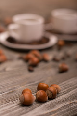 two small white cups of coffee with cocoa beans, slices of chocolate and hazelnuts on wooden background