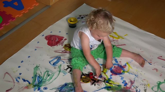 Happy baby girl painting her face with colorful fingers paint
