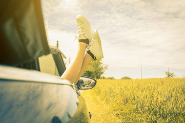 Young cool girl with shoes out of the automobile window to enjoy the view in summertime