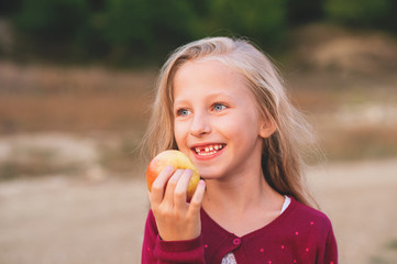 Losing baby teeth. Preteen child loosing teeth. Cut girl smailing.Closeup portrait of happy child eating yelow apple outdoors in autumn.
