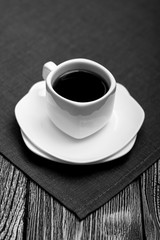 small white cup of coffee on fabric on wooden background. Black and white