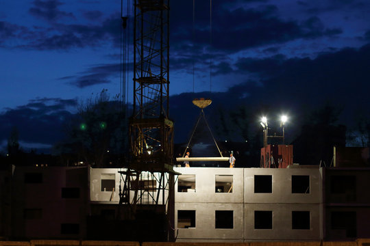 Crane downs slab, workers on building under construction at nigh