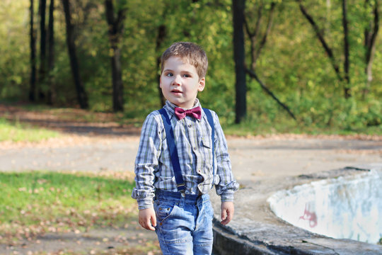Smiling little boy with bow tie and jeans poses in sunny green p