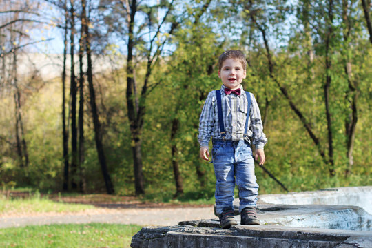 Smiling little boy with bow tie and jeans stands in sunny green