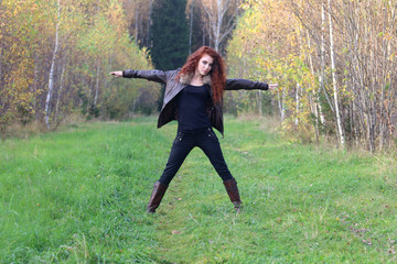 Pretty young woman in leather jacket poses on grass in autumn fo