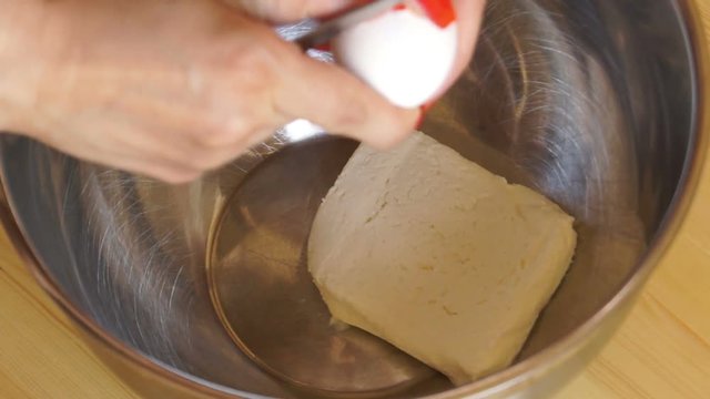 Woman breaks an egg and mixes it with cream cheese in a metal bowl