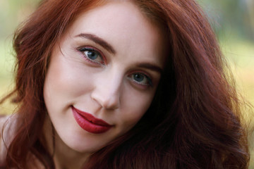 Fototapeta premium Woman with red hair smiles in forest, shallow dof, close up