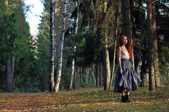 Beautiful woman stands on dry leaves in skirt in autumn forest