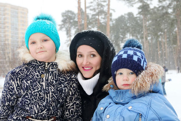 Happy family (mother, daughter, son) pose during snowfall in win