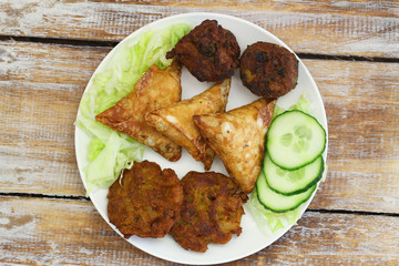 Plate full of Indian snacks including samosas, onion bhajis and pakoras on rustic wooden surface
