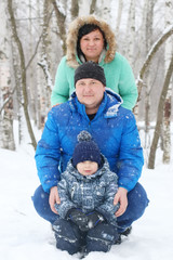 Happy mother, father and son pose on snow during snowfall at win